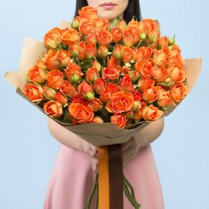 A woman holding a vibrant bouquet of orange roses, showcasing a beautiful hand arrangement of flowers.