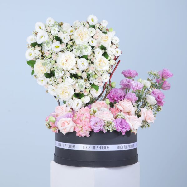 A black box filled with white flowers and pink roses offers a beautiful contrast and an appealing visual aesthetic in a heart-shaped arrangement.