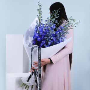 A woman presents a lovely bouquet of blue flowers, capturing the essence of nature's beauty in her gentle embrace.