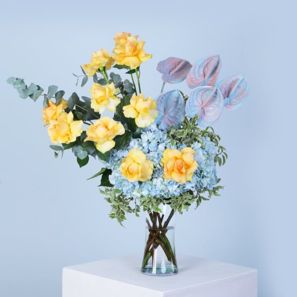 A decorative vase filled with cheerful yellow roses and elegant blue hydrangeas, offering a fresh and lively aesthetic.