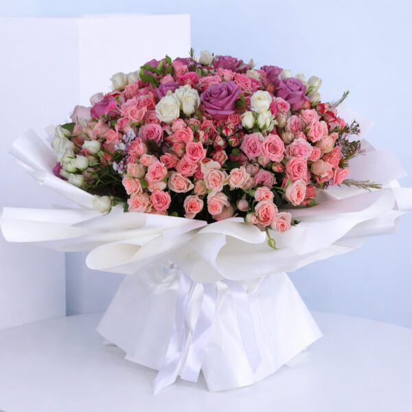 A delightful bouquet of pink and purple roses resting on a white table adding a touch of elegance to the setting.
