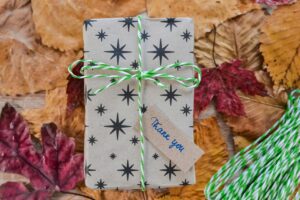 A gift wrapped in brown paper with a star pattern and tied with a green and white twine bow.