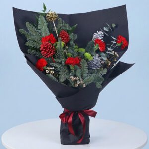 A modern Christmas bouquet with red carnations, silver accents, and lush greenery wrapped in black paper with a red ribbon.