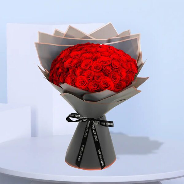 A large bouquet of 50 red roses wrapped in gray paper with a black ribbon and a gold accent.