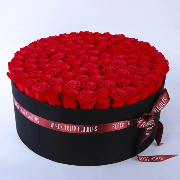 A large black round box filled with 50 red roses tied with a maroon ribbon on the side.