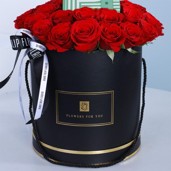 A black round box filled with red roses accompanied with a box of Patchi chocolates.