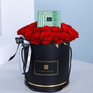 A black round box filled with red roses accompanied with a box of Patchi chocolates.