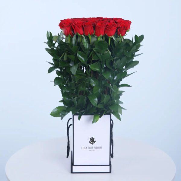 A easy-to-carry stylish white bag filled with 15 red roses with green leaves.