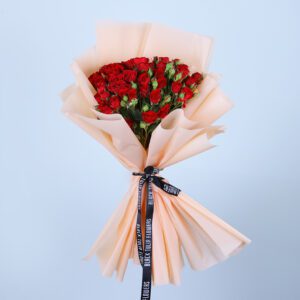 A bouquet of 20-Stem Red Spray Roses elegantly arranged in a peach wrap tied with a black ribbon.