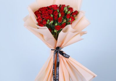 A bouquet of 20-Stem Red Spray Roses elegantly arranged in a peach wrap tied with a black ribbon.