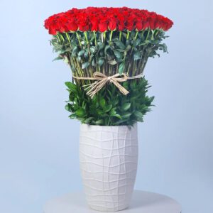 A large white vase filled with 200 red roses and greenery.