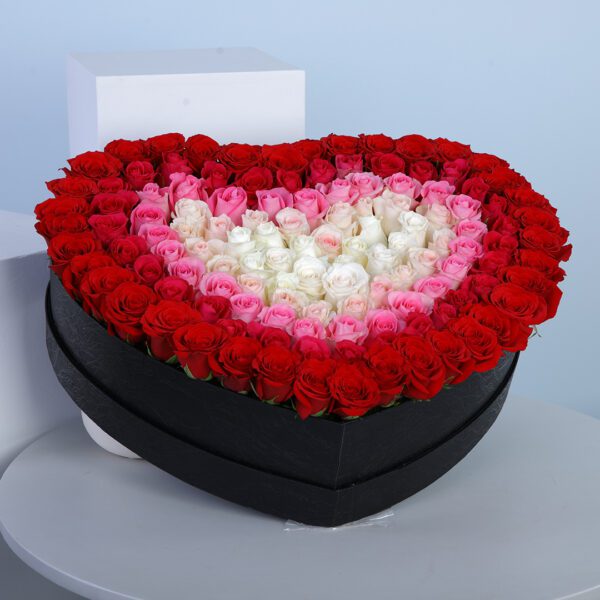 A heart-shaped box filled with layers of red, pink, and white roses.