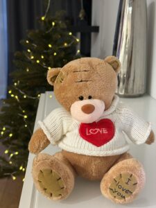 The image shows a brown teddy bear wearing a white sweater with a red heart on it that says "Love".