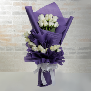 A bouquet of approximately a dozen pristine white roses is elegantly wrapped in layers of deep purple paper