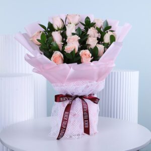 A stunning bouquet of peach roses and greenery, presented in pink wrapping with a striking dark red ribbon.