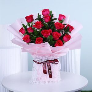 Soft pink roses elegantly wrapped in matching pink paper and airy white netting, topped off with a bold dark red ribbon.