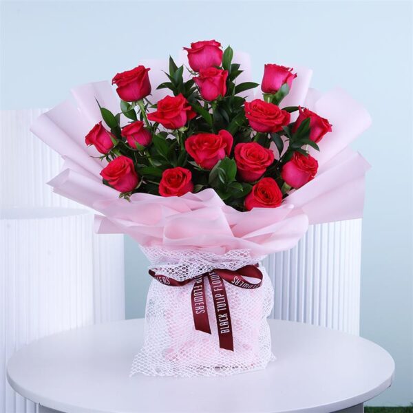 Soft pink roses elegantly wrapped in matching pink paper and airy white netting, topped off with a bold dark red ribbon.