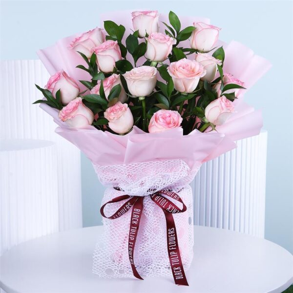 A lovely bouquet of pale blush pink roses wrapped in soft pink paper and delicate white netting, tied with a rich burgundy ribbon.