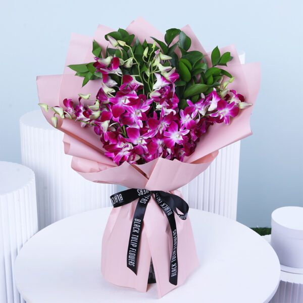 A purple orchid bouquet with ruscus in pink wrap tied with black ribbon.