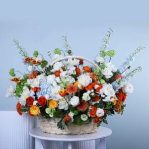 A woven basket overflowing with a colorful assortment of flowers in shades of white, orange, yellow, blue, and green, with visible green foliage.