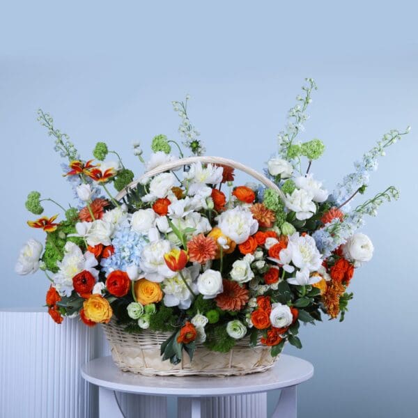 A woven basket overflowing with a colorful assortment of flowers in shades of white, orange, yellow, blue, and green, with visible green foliage.