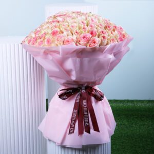A bouquet of pastel pink roses with deeper pink edges, wrapped in soft pink paper and tied with a dark maroon ribbon.