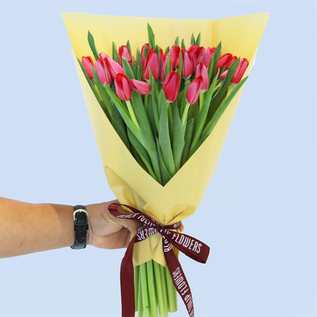 Bouquet of fresh red tulips wrapped elegantly in yellow and tied with maroon ribbon.
