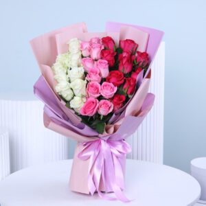 A vibrant bouquet of white, light pink,and hot pink roses arranged and wrapped in layers of light pink and lavender paper, tied with a soft lavender ribbon.