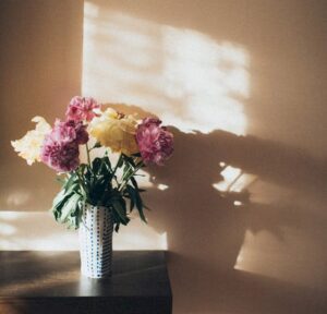 a beautiful bouquet of flowers in a dark green vase, set against a backdrop of a light brown wall.
