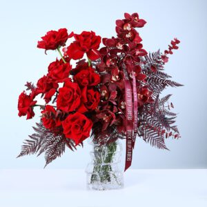 20 red rose & Cymbidium flowers with green leaves arranged in a clear glass vase