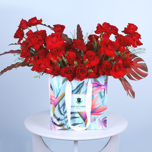 Romantic bouquet featuring fresh red roses and delicate green foliage in a stylish bag.