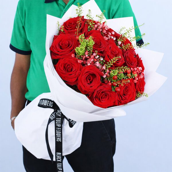 Valentine floral arrangement with red roses and filler flowers wrapped in a white sheet and tied with a black satin ribbon