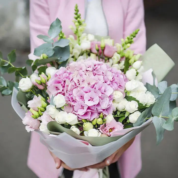 A woman dressed in casual attire, holding a fresh bouquet of assorted flowers.